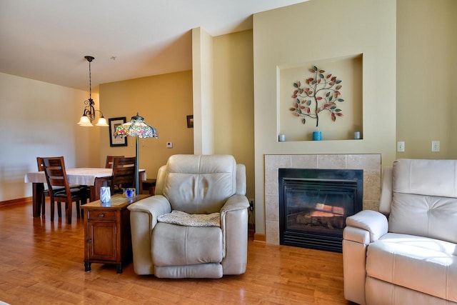 living room featuring baseboards, light wood-style flooring, and a tiled fireplace