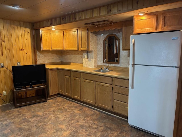 kitchen with a sink, wood walls, light countertops, and freestanding refrigerator