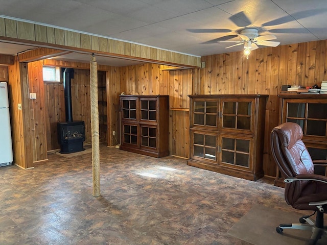 unfurnished office with tile patterned floors, wooden walls, a wood stove, and a ceiling fan