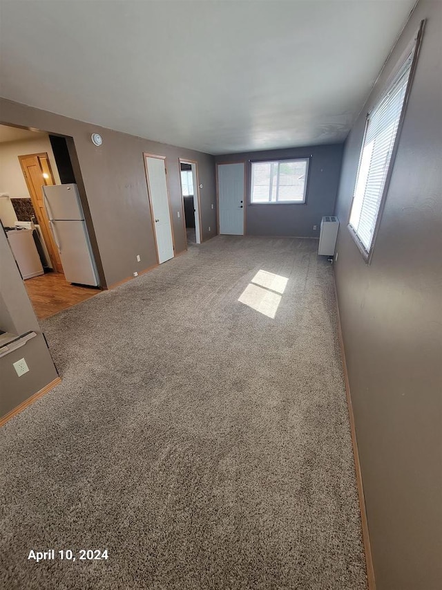 unfurnished living room with radiator, baseboards, and light colored carpet