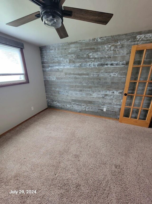 carpeted spare room featuring wood walls and a ceiling fan