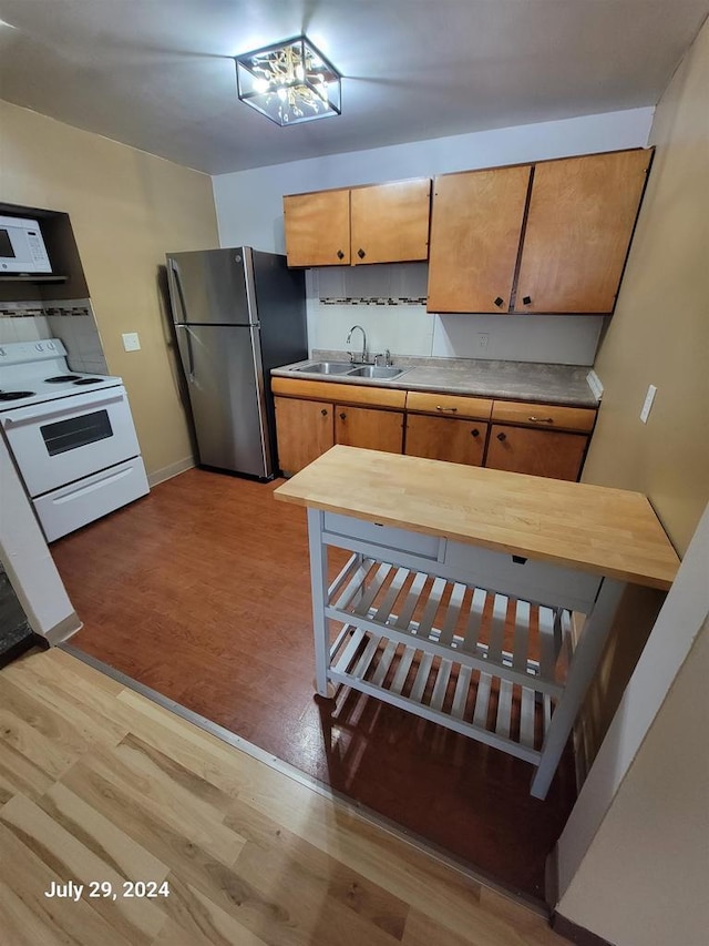 kitchen with white appliances, brown cabinetry, baseboards, light wood finished floors, and a sink