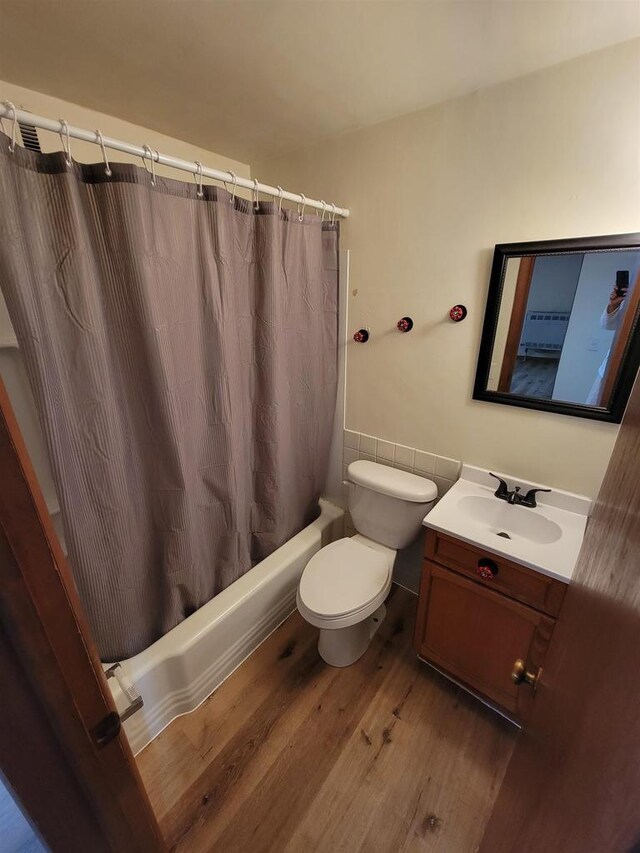 bathroom with shower / bathtub combination with curtain, toilet, wood finished floors, and vanity