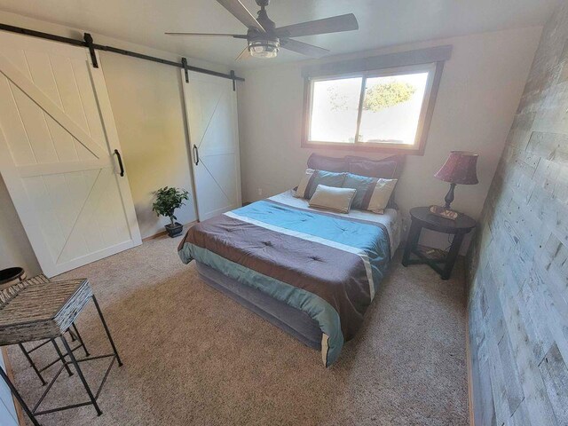 carpeted bedroom featuring a barn door and ceiling fan