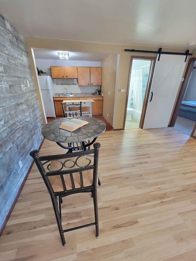 kitchen featuring light wood-type flooring, a sink, freestanding refrigerator, a barn door, and light countertops