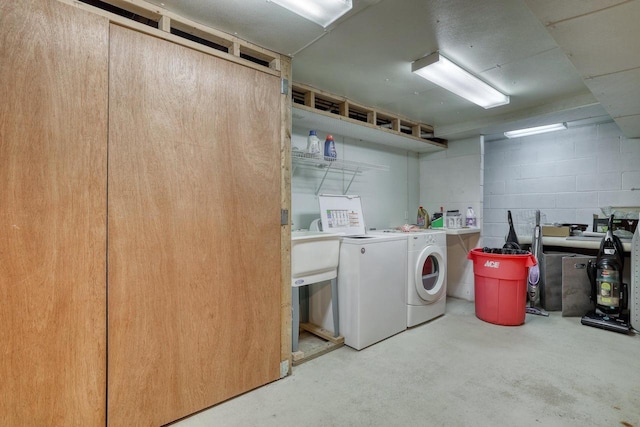 washroom featuring a sink, concrete block wall, and washer and clothes dryer