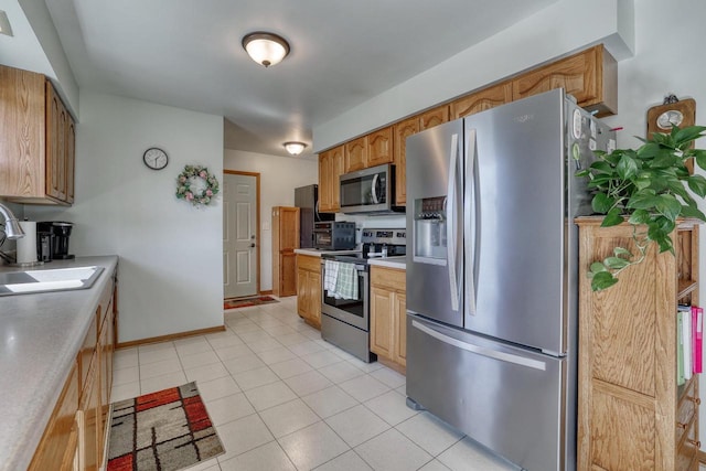 kitchen with baseboards, light countertops, light tile patterned floors, appliances with stainless steel finishes, and a sink