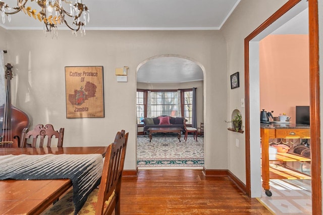 dining space with wood finished floors, baseboards, arched walkways, ornamental molding, and a notable chandelier