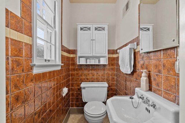 bathroom with visible vents, a wainscoted wall, toilet, a sink, and tile walls