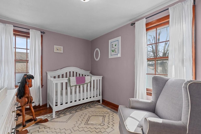 bedroom with a nursery area, wood finished floors, and baseboards