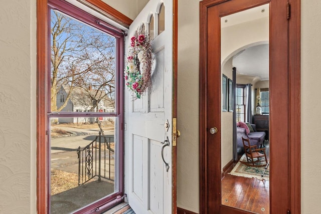 foyer entrance with arched walkways, wood finished floors, and a textured wall