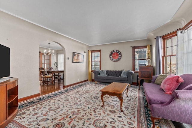 living room featuring a notable chandelier, ornamental molding, wood finished floors, arched walkways, and baseboards