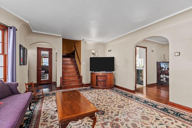 living room with ornamental molding, wood finished floors, arched walkways, baseboards, and stairs