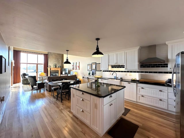 kitchen with backsplash, dark countertops, freestanding refrigerator, light wood-style floors, and wall chimney range hood