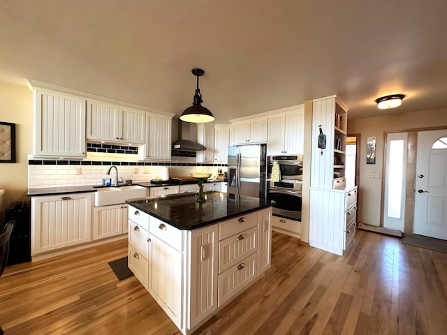 kitchen featuring light wood finished floors, open shelves, a sink, appliances with stainless steel finishes, and wall chimney exhaust hood