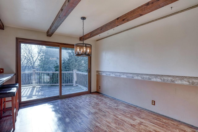 unfurnished dining area featuring beamed ceiling, a notable chandelier, and wood finished floors