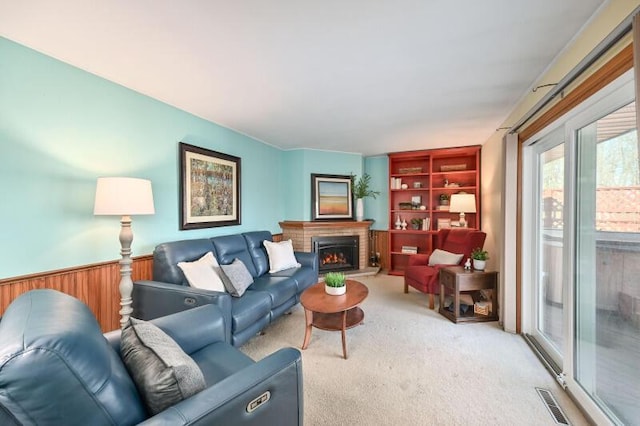 living room featuring wooden walls, visible vents, a wainscoted wall, a fireplace, and light carpet