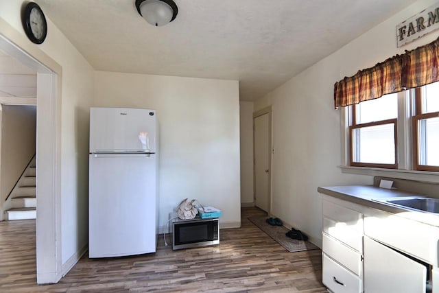 kitchen with baseboards, freestanding refrigerator, light wood-style floors, white cabinetry, and stainless steel microwave