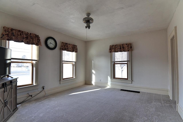 carpeted spare room featuring a textured ceiling and baseboards