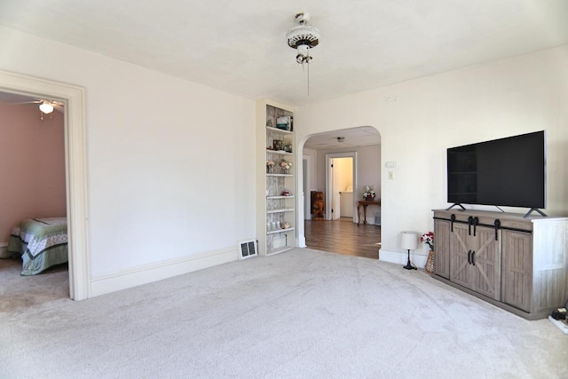 living area with a ceiling fan, visible vents, carpet, baseboards, and arched walkways