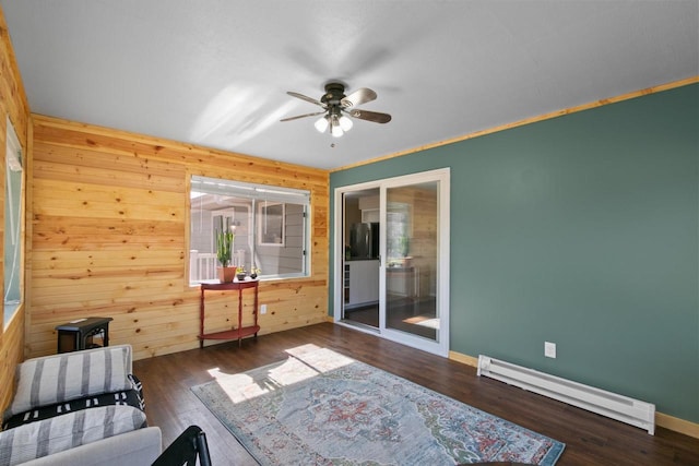 living area with wood finished floors, wood walls, baseboard heating, and ceiling fan