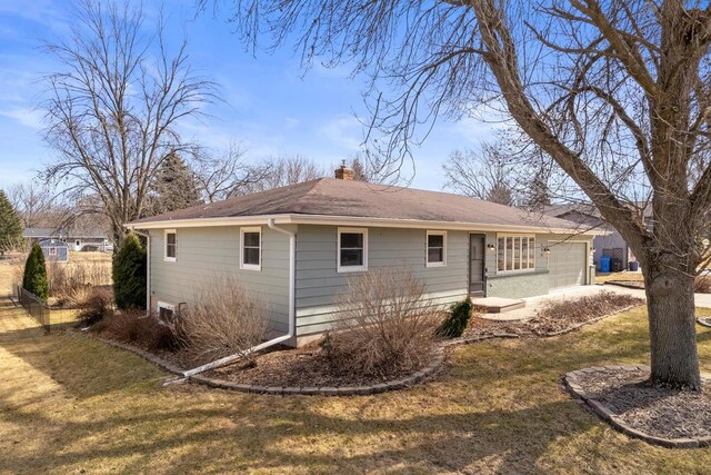 back of property with an attached garage, a chimney, and a lawn