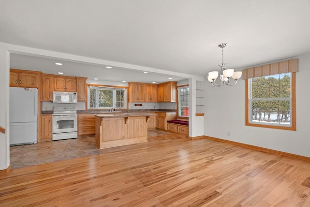 kitchen with baseboards, a chandelier, a breakfast bar, light wood-style flooring, and white appliances