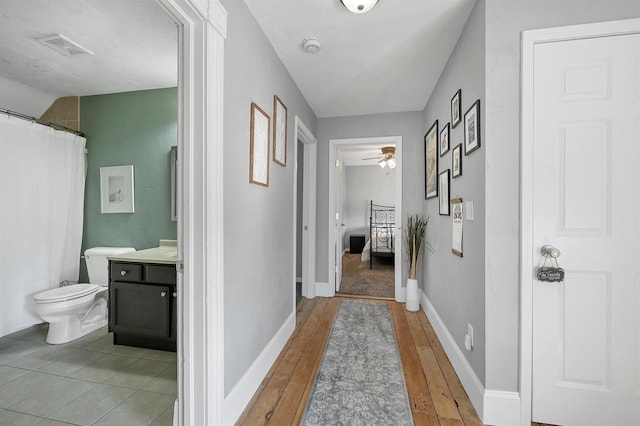 hall featuring visible vents, baseboards, and light wood finished floors