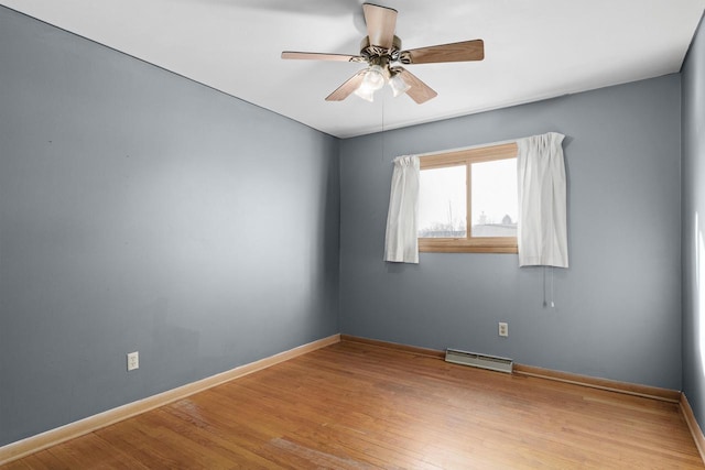 unfurnished room featuring a ceiling fan, a baseboard heating unit, baseboards, and wood finished floors