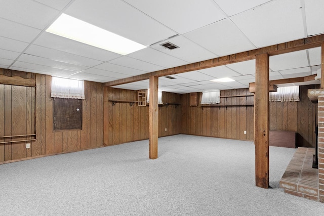 basement featuring a drop ceiling, visible vents, wooden walls, and carpet flooring