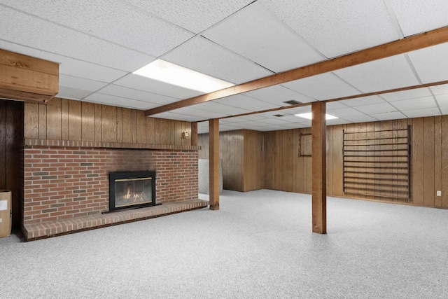 finished basement featuring carpet, visible vents, a fireplace, a paneled ceiling, and wood walls