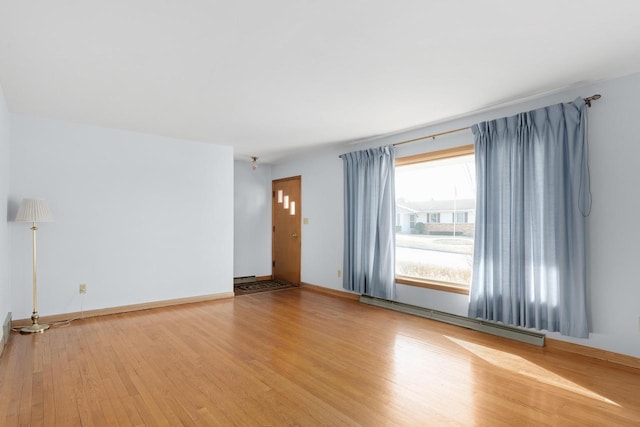 unfurnished room featuring baseboard heating, light wood-type flooring, and baseboards