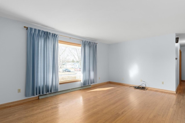 empty room featuring a baseboard heating unit, wood finished floors, and baseboards