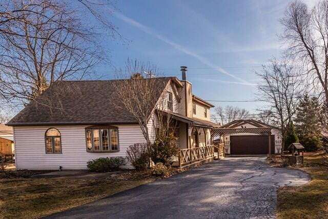 view of side of property with an outbuilding, a chimney, a detached garage, and roof with shingles