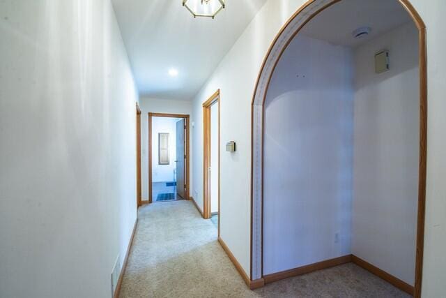 hallway featuring light colored carpet, arched walkways, and baseboards