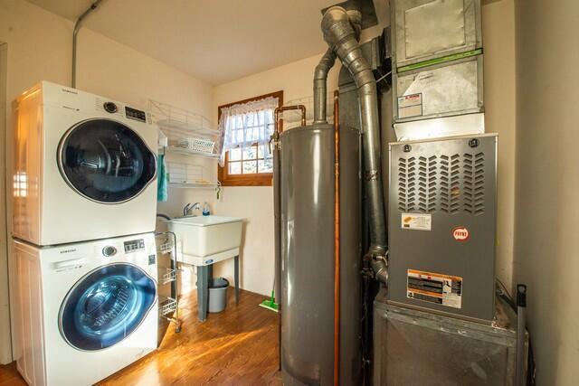 washroom featuring laundry area, gas water heater, stacked washer / drying machine, and wood finished floors