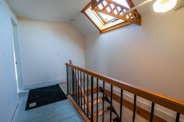 hall featuring lofted ceiling with skylight, wood finished floors, an upstairs landing, and baseboards