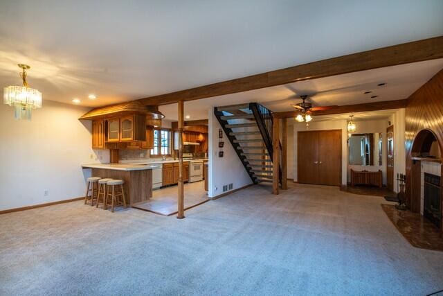 unfurnished living room with stairway, light carpet, beamed ceiling, and a fireplace with raised hearth