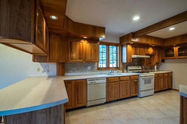 kitchen with beamed ceiling, brown cabinets, under cabinet range hood, white appliances, and light countertops