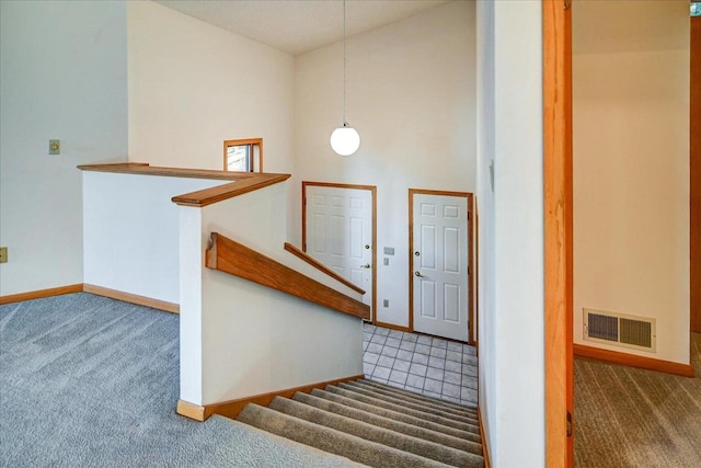 staircase with visible vents, carpet flooring, baseboards, and a towering ceiling