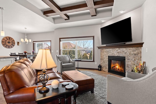 living area with light wood-type flooring, beam ceiling, coffered ceiling, a stone fireplace, and an inviting chandelier