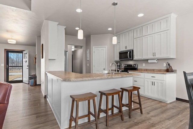 kitchen with a kitchen breakfast bar, appliances with stainless steel finishes, light wood-style floors, white cabinetry, and a sink