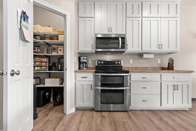 kitchen with white cabinets, appliances with stainless steel finishes, light countertops, and light wood-style floors