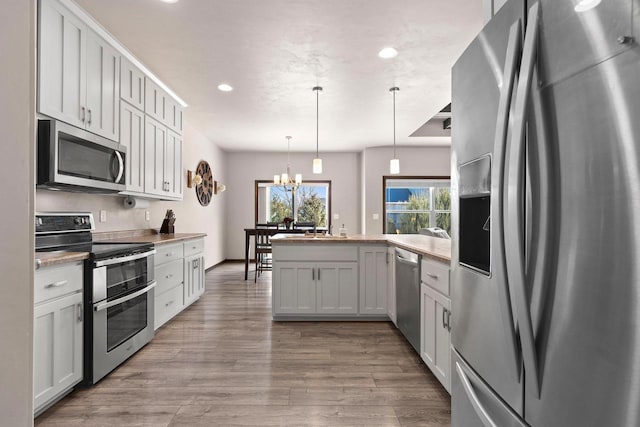 kitchen with a chandelier, light wood-style flooring, a peninsula, hanging light fixtures, and stainless steel appliances