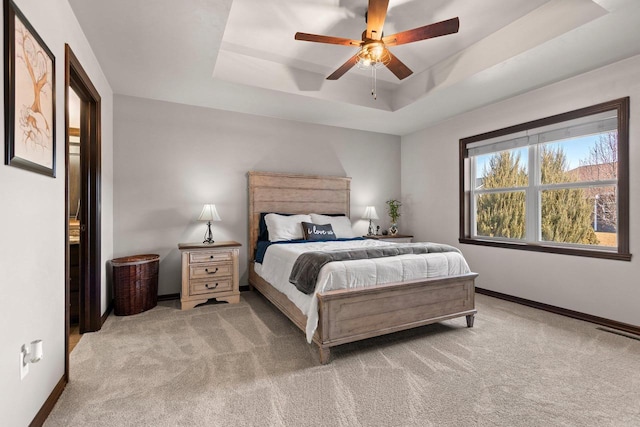 carpeted bedroom with a ceiling fan, a raised ceiling, visible vents, and baseboards