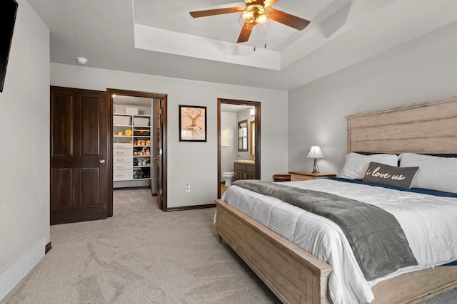 bedroom featuring a tray ceiling, a spacious closet, light colored carpet, and baseboards