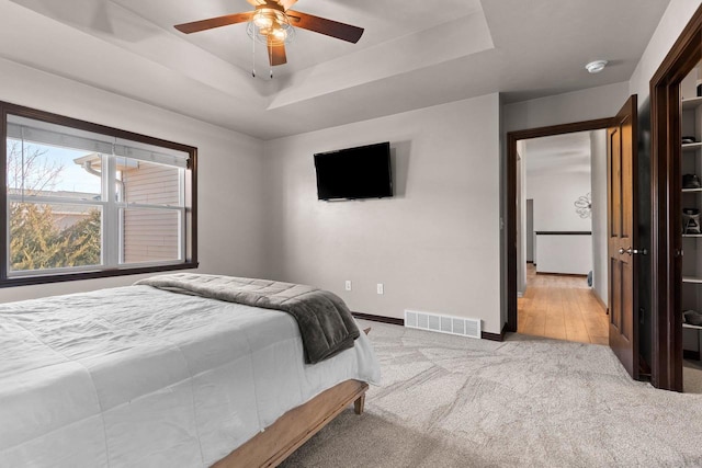 carpeted bedroom featuring a tray ceiling, visible vents, baseboards, and a ceiling fan