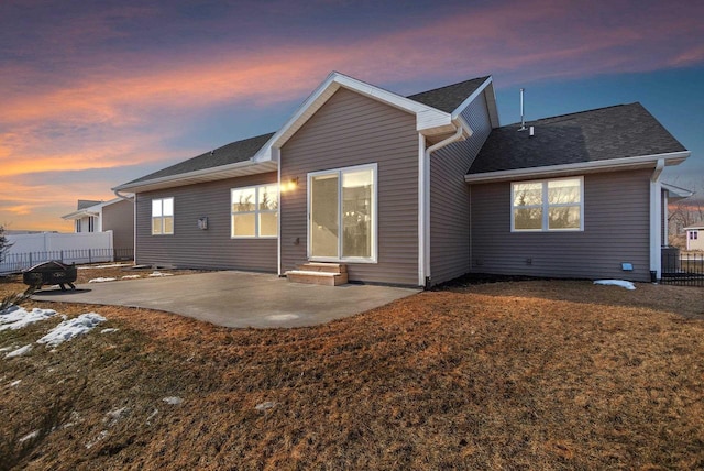 back of property at dusk featuring a patio area, a yard, roof with shingles, and fence