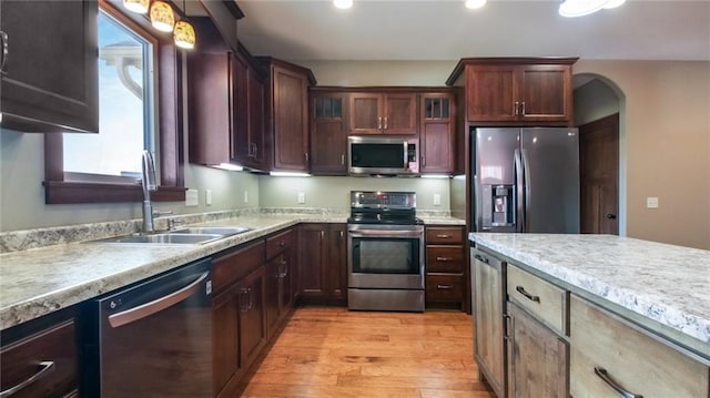 kitchen featuring light wood-type flooring, light countertops, arched walkways, stainless steel appliances, and a sink