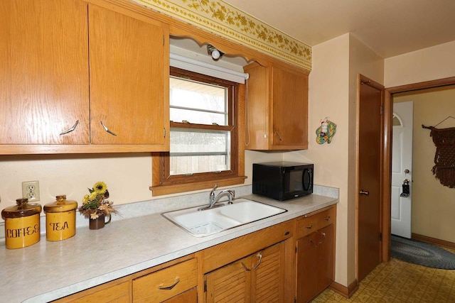 kitchen with baseboards, black microwave, light countertops, brown cabinetry, and a sink